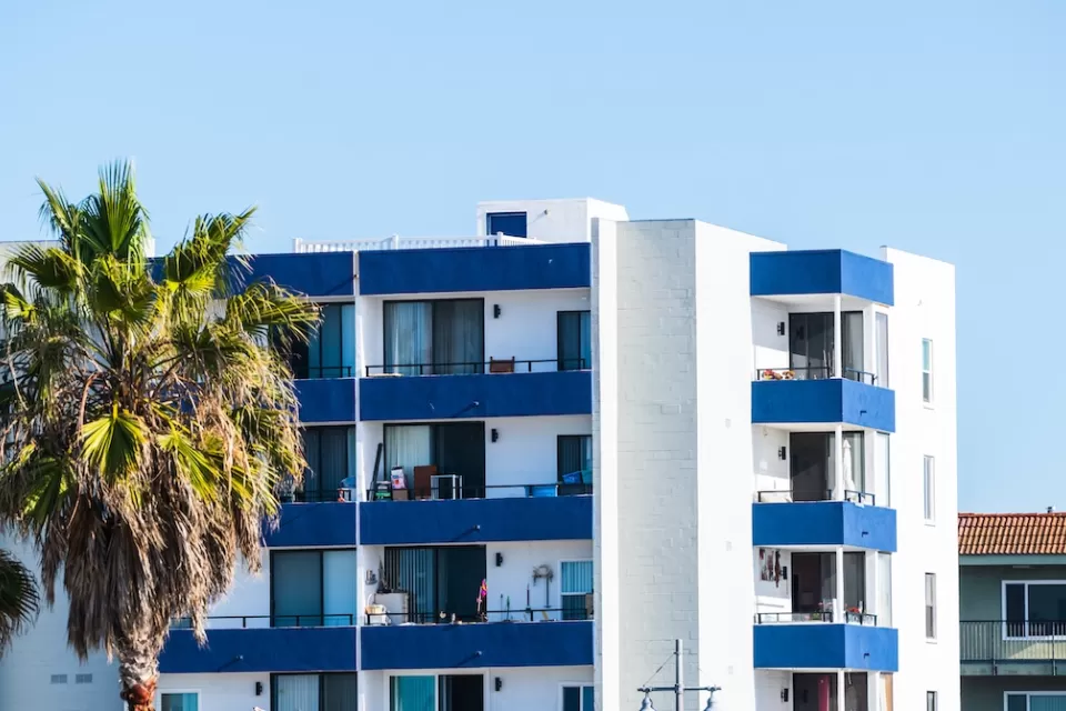 Top floors of blue and white apartment building with palm trees against sunny blue sky in Malibu, California.